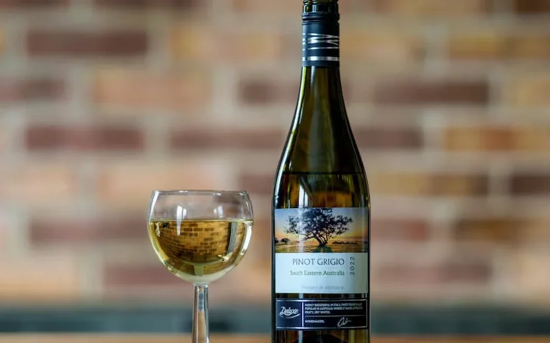 A bold Bordeaux wine bottle with a golden label placed on a dark wooden table under soft afternoon light.