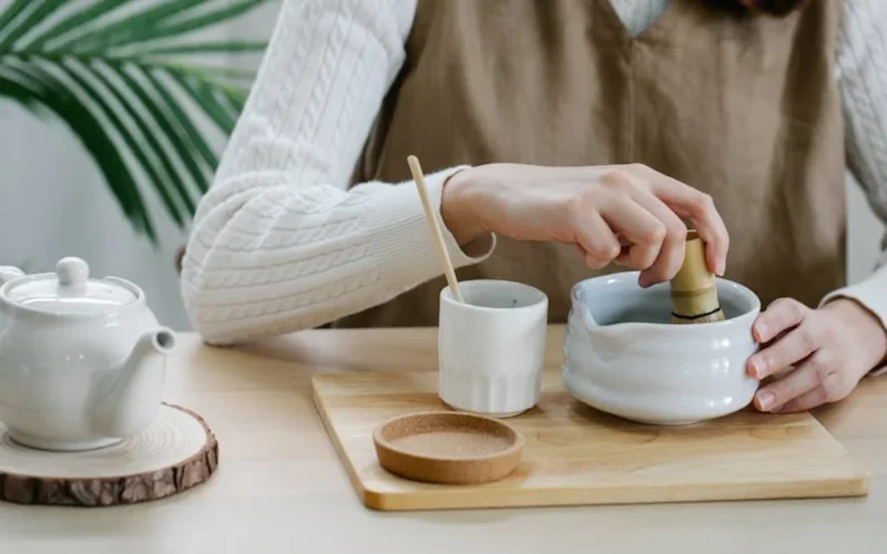 A dark wood table with a steaming Puer tea cup and a frothy iced matcha latte under soft golden light.