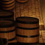 Rick Arline pours wine into a crystal glass in front of an oak barrel with natural light.