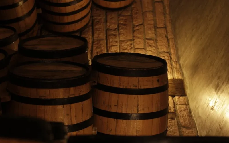 Rick Arline pours wine into a crystal glass in front of an oak barrel with natural light.
