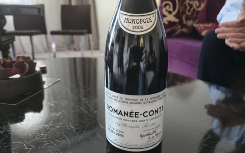 Dusty Romanée-Conti bottle with intact cork on dark wooden table under warm lighting