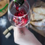 Clear 0% rosé wine poured into stemmed glass under soft golden lighting in minimalist kitchen with greenery.