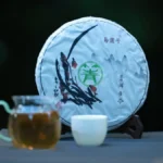 Close-up of pu'er tea cake on dark tray with tea leaves and teapot under warm light.