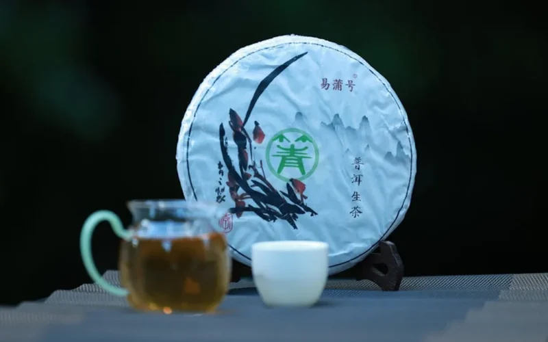 Close-up of pu'er tea cake on dark tray with tea leaves and teapot under warm light.