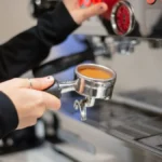 Barista operating Lelit espresso machine with dark roast coffee flowing into a steel cup.