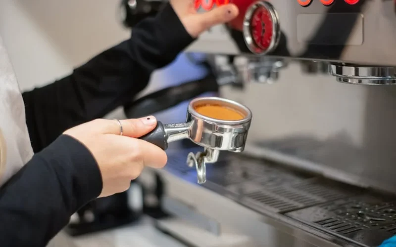 Barista operating Lelit espresso machine with dark roast coffee flowing into a steel cup.