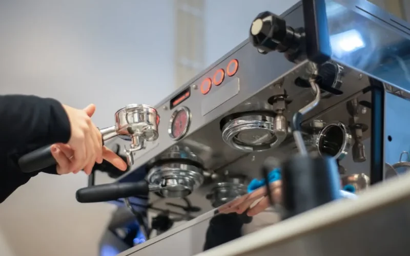 Two high-end espresso machines side by side in a modern coffee bar with steam rising and light reflecting off their surf
