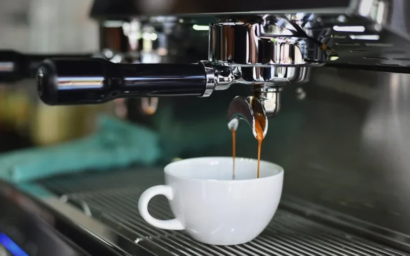 Superautomatic espresso machine steaming as barista prepares coffee in modern kitchen.