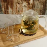 Clay teapot with steam rising over wooden tray and dried herbs on aged bamboo shelves.