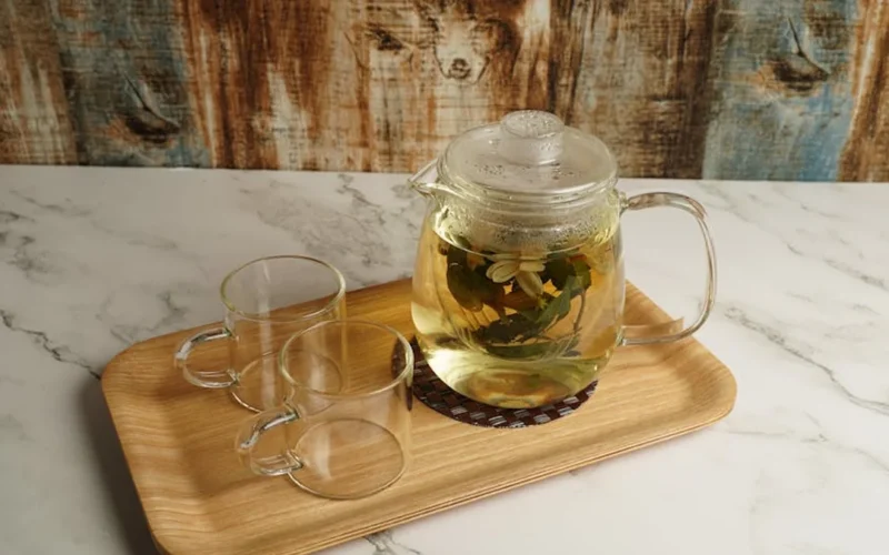 Clay teapot with steam rising over wooden tray and dried herbs on aged bamboo shelves.