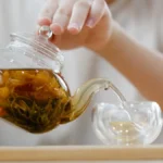 Dark pu'er tea leaf unfolding in a clay teapot with steam rising under warm lighting.