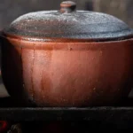 A clay pot filled with steeping tea leaves emitting steam under warm lighting.