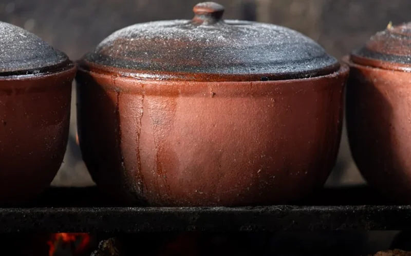 A clay pot filled with steeping tea leaves emitting steam under warm lighting.