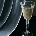 A golden champagne flute filled with sparkling wine, reflecting light on a rustic wooden table with a vintage book and f