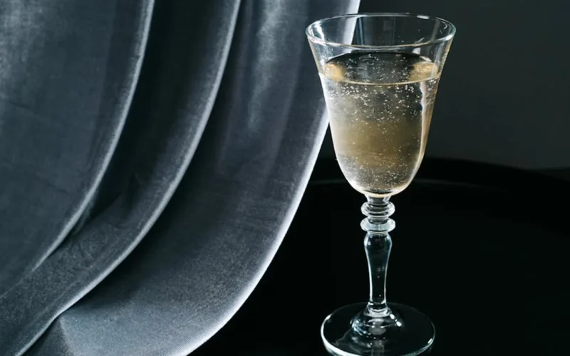 A golden champagne flute filled with sparkling wine, reflecting light on a rustic wooden table with a vintage book and f