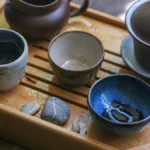 A traditional tea ceremony setup with a steaming teapot and cup on a bamboo tray.