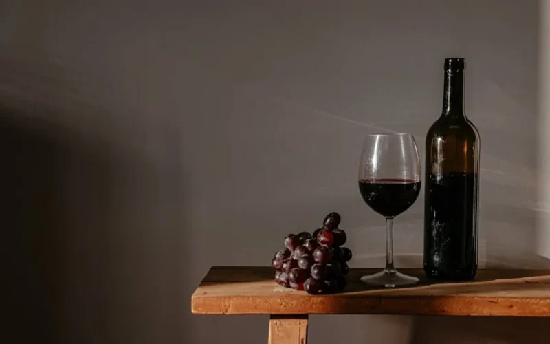 Aged tawny port wine bottle on rustic table with dried grapes and elegant label.