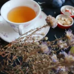 Golden tea leaves steeping in porcelain cup with steam rising under warm lighting.