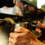 Aeropress brewing with steam rising from hot water into glass container under warm lighting.