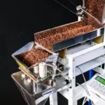Thermocouple probe in coffee roaster with digital displays and tools on wooden work surface.