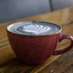 A steaming coffee mug on a wooden table under a sunrise with coffee beans and a clock nearby.