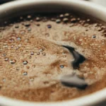 A steaming coffee cup with Trader Joe's label in a sunlit kitchen, dark liquid swirling with light reflections.