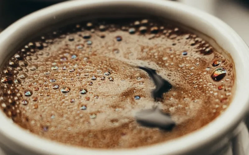 A steaming coffee cup with Trader Joe's label in a sunlit kitchen, dark liquid swirling with light reflections.