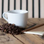 Coffee beans spilling from a ceramic jar on a wooden table with natural light casting shadows.