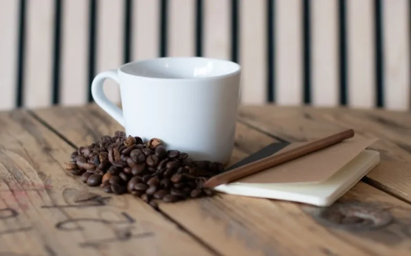 Coffee beans spilling from a ceramic jar on a wooden table with natural light casting shadows.