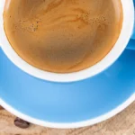 Espresso pouring into cappuccino cup with steam and natural light.