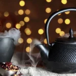 A glass teapot filled with shimmering black tea leaves and rising steam under warm lighting.