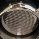 Espresso machine steaming milk into glass cup with warm lighting on marble surface.