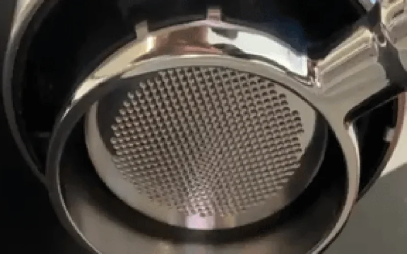 Espresso machine steaming milk into glass cup with warm lighting on marble surface.