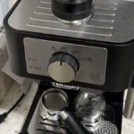 Espresso shot pouring into dark roast cup on black espresso machine under warm lighting.