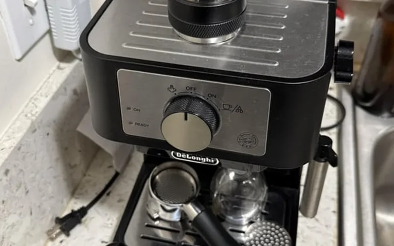Espresso shot pouring into dark roast cup on black espresso machine under warm lighting.