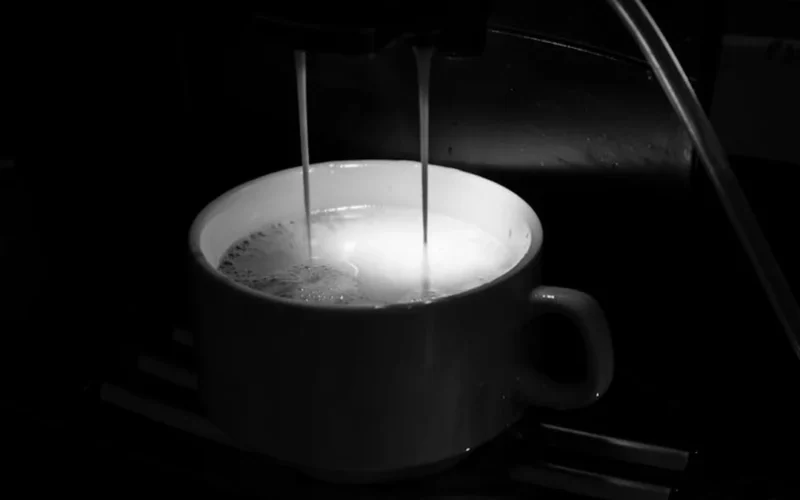 Dark espresso dripping into black ceramic cup with steam and shadowy lighting.
