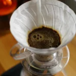 Artisanal borosilicate pour over coffee brewing setup with steam rising under soft lighting.
