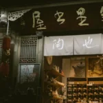 A steaming clay gaiwan of dark puerh tea in a traditional tea room with bamboo and calligraphy scrolls.