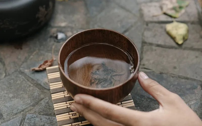 Young autumn pu er tea leaves swirling in clay teapot with steam rising under golden light.