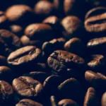 A ceramic bowl holds a mix of dark and light roasted coffee beans under warm golden light.
