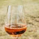 Red wine pouring into a glass on a wooden table with vineyard background.