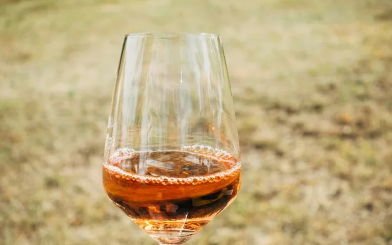Red wine pouring into a glass on a wooden table with vineyard background.