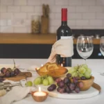 Decanted Bordeaux wine in crystal glass under candlelight on a wooden table with wine bottles and tasting notes.