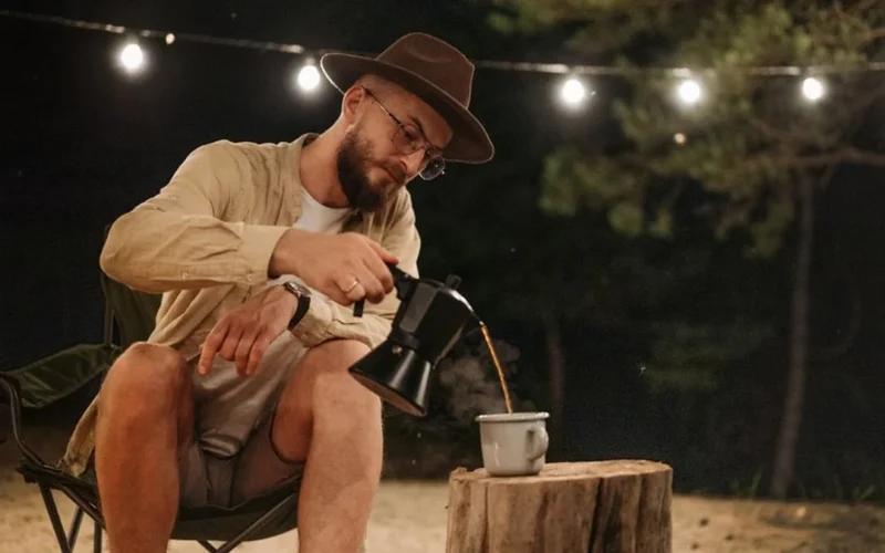Group of professionals gathering around a campfire with coffee mugs in a wooded setting.