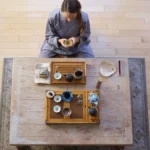 Steaming tea in a ceramic gaiwan on a rustic wooden surface with loose tea leaves.