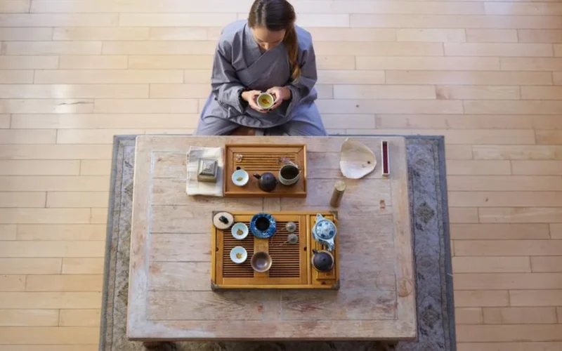Steaming tea in a ceramic gaiwan on a rustic wooden surface with loose tea leaves.