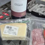 Red wine poured into glasses next to Italian meats and cheeses on wood.