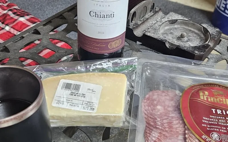 Red wine poured into glasses next to Italian meats and cheeses on wood.