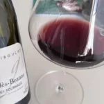 A glass of red Burgundy wine on a wooden table in warm lighting.