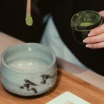 Close up of steaming dark puerh tea being poured into a traditional clay cup.